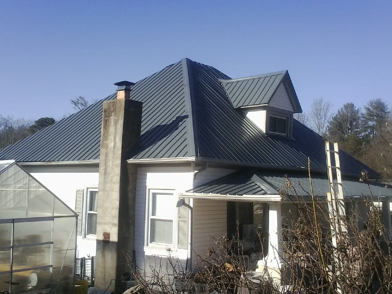Dark blue standing seam metal roof on a white farmhouse with dormer — Slate & Tile Roof Repair by Roofing Brothers in Ogdensburg