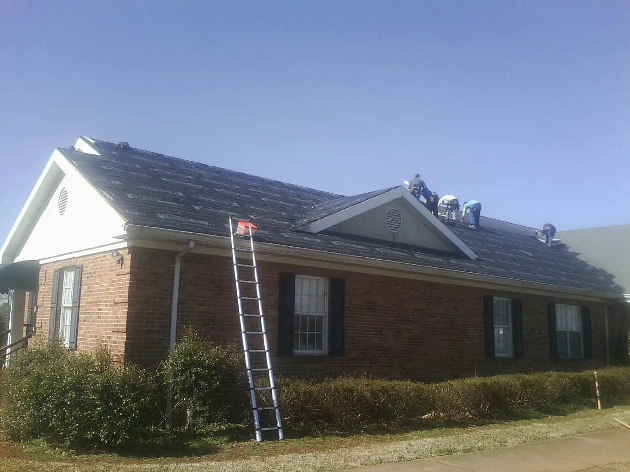 Crew tearing shingles off a brick ranch roof with a ladder set — Emergency Roof Repair work by our crew in Ogdensburg