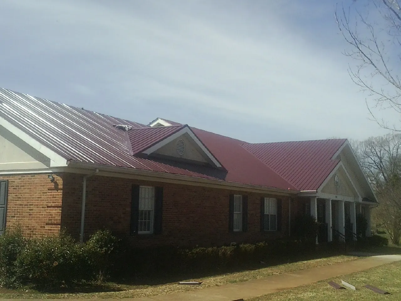 Red metal roof with gabled entries on a long brick building, from a Hail Damage Roof Repair job in Ogdensburg
