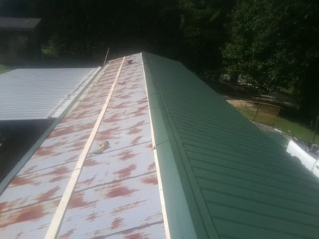 Old rusted panels beside newly installed green metal roofing — Wind Damage Roof Repair by Roofing Brothers in Ogdensburg