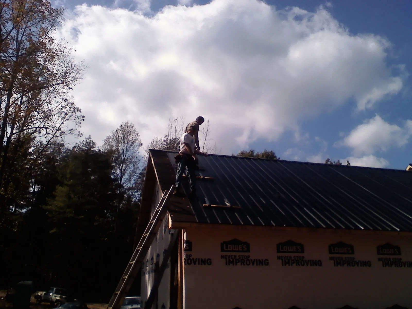 Roofer fastening dark metal panels high against a cloudy sky, from a Roof Inspection job in Ogdensburg