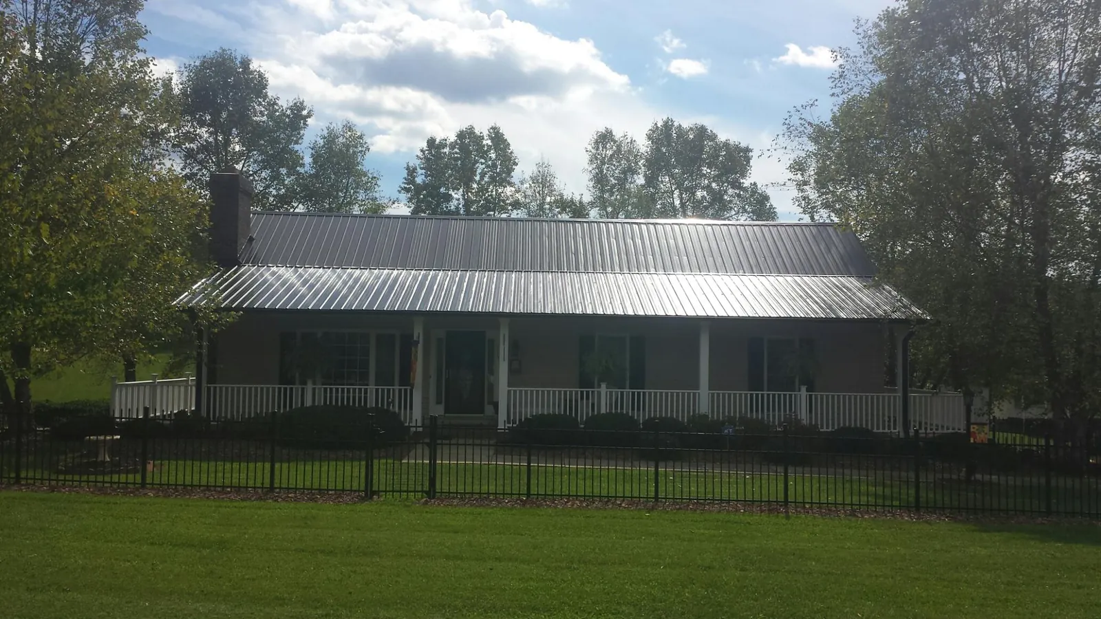 Gray metal roof on a brick ranch with a full width front porch — Gutter Guard Installation work by our crew in Ogdensburg