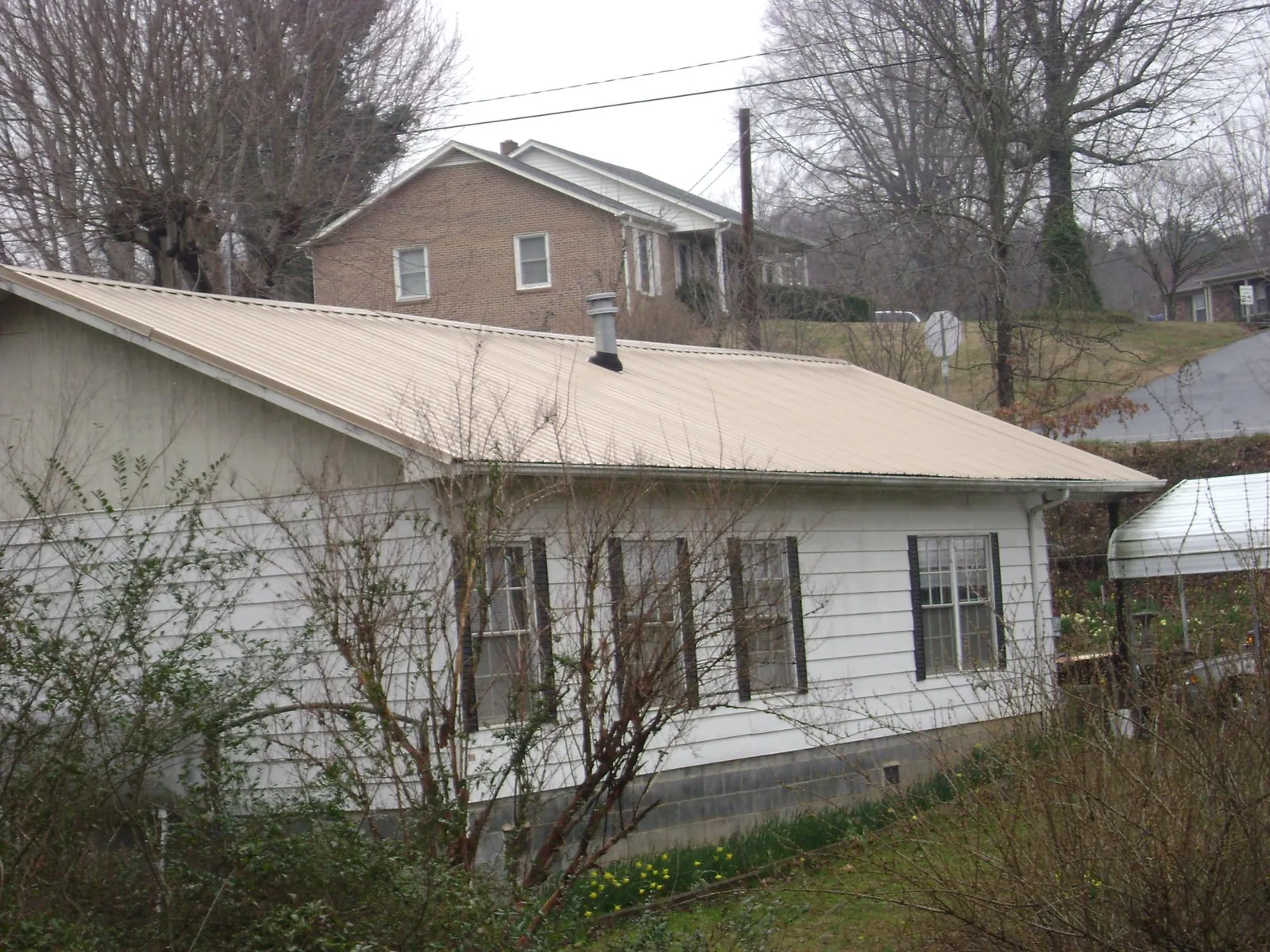 Tan metal roof on a white sided house set into a hillside — Commercial Roofing by Roofing Brothers in Ogdensburg